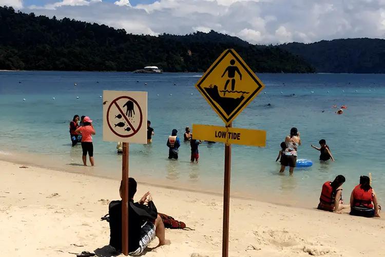 Tourists reading a beach safety warning sign in the Andaman Islands